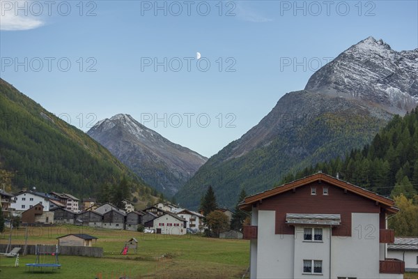 A mountain village with scattered houses in a valley between high mountains under a clear sky with a crescent moon, Saas Fee, Switzerland, Europe