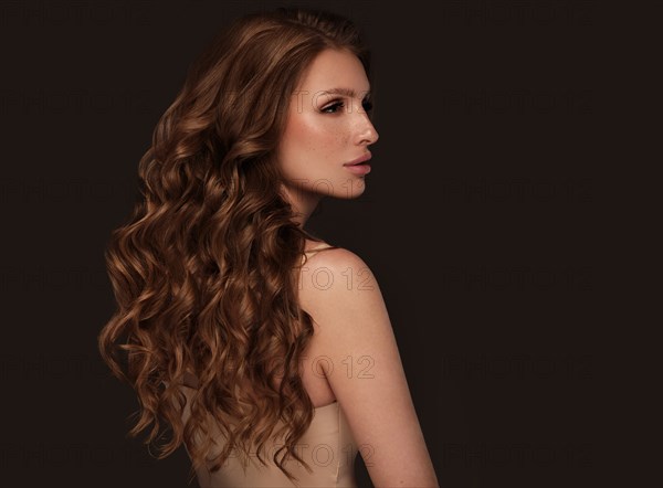 Beautiful brown-haired girl with a perfectly curls hair, and classic make-up. Beauty face and hair. Picture taken in the studio