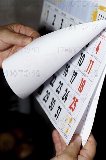 Unrecognizable woman's hands turning the pages of a calendar against a dark background