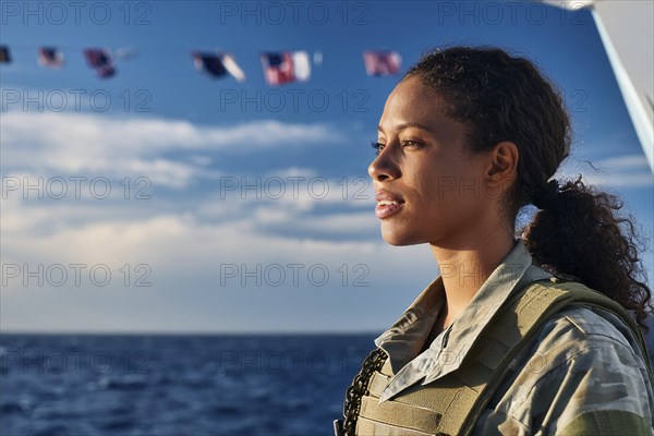 Woman in military uniform looking at the sea, with waving flags of the ship in the background, AI generated, AI generated