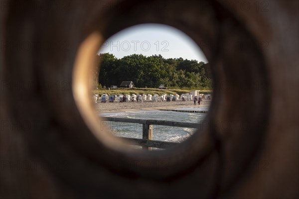 View through a round wooden hole onto a beach with beach chairs and green trees in the background, Zingst, Mecklenburg-Vorpommern, Germany, Europe