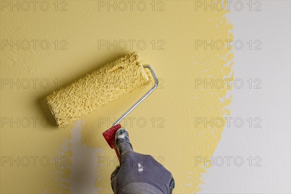 Wall is painted with yellow paint, hand with paint roller