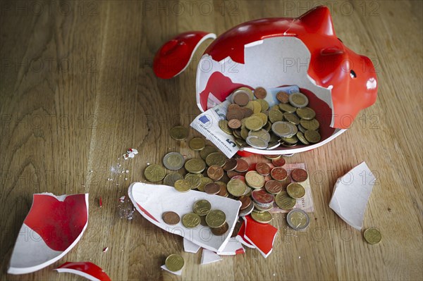 Symbolic photo on the subject of saving. An open, broken piggy bank with coins and banknotes stands on a table. Berlin, 10.02.2024