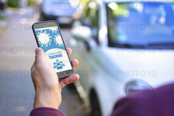 Corona Virus Tracking App concept with hand holding cell phone with application design on screen in front of blurry street background