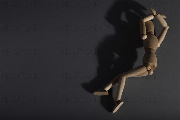 Wooden mannequin lies in a protective position on gray background. loneliness, violence, vulnerability, depression disorder concept. copy space, hard light