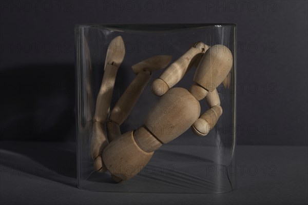 Wooden mannequin locked in a glass cube on gray background. captivity, break rules, loneliness, depression disorder concept. close up