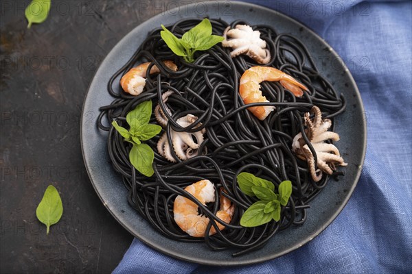 Black cuttlefish ink pasta with shrimps or prawns and small octopuses on black concrete background and blue textile. Top view, close up, selective focus