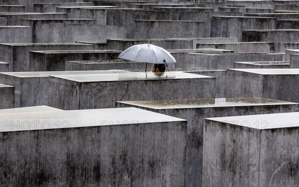 A visitor to the Memorial to the Murdered Jews of Europe protects himself from heavy rain with an umbrella. Berlin, 23.06.2023