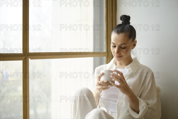 Woman sitting by the window looking into a cup of tea or coffee