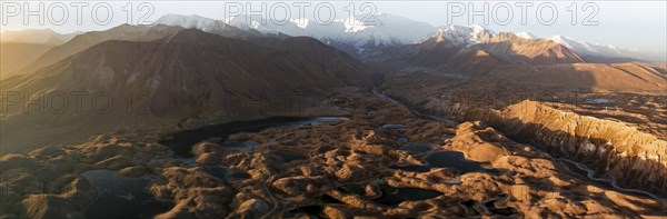 PanoramaWhite glaciated and snow-covered mountain peak Pik Lenin at sunrise, hilly landscape with golden yellow meadows and lakes, aerial view, Trans Alay Mountains, Pamir Mountains, Osher Province, Kyrgyzstan, Asia