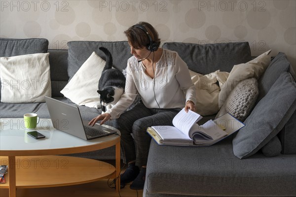 Woman, mid-50s, works from home, with laptop and communicates with colleagues via headset, home office, on the sofa