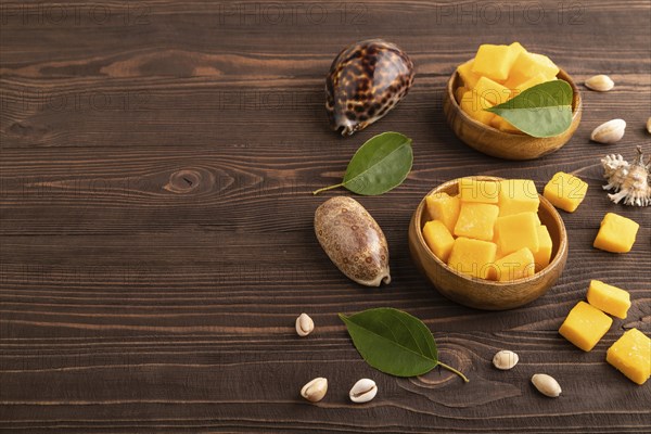 Dried and candied mango cubes in wooden bowls on brown wooden textured background. Side view, copy space, vegan, vegetarian food concept