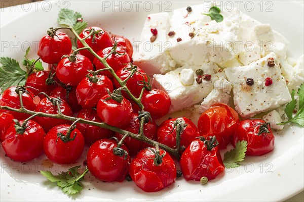 Baked cherry tomatoes, with cheese, and spices, on a white plate, homemade, no people