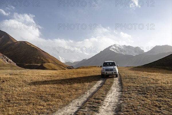 Off-road vehicle on a track between yellow meadows, glaciated high mountain peaks in the background, Lenin Peak, Trans Alay Mountains, Pamir Mountains, Osh Province, Kyrgyzstan, Asia