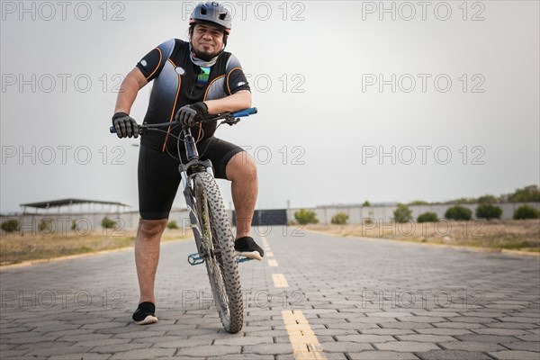 Smiling cyclist on his bike looking at the camera on the road. Chubby male cyclist in sportswear riding a bicycle outdoors