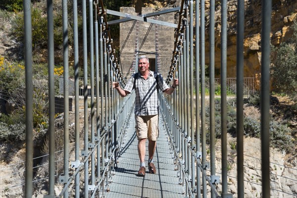 Man on a metal suspension bridge, surrounded by rocks and nature in daylight, Congost de Mont-rebei gorge, Noguera Ribagorçana Mont-rebei Natural Park, Montsec mountain range, Noguera Ribagorçana river, Lleida province, Catalonia, Aragon, Spain, Europe