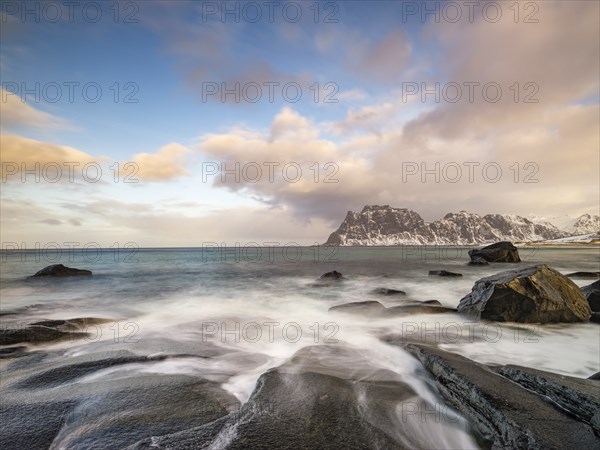 Smoothly polished rocks on Utakleiv beach in a dramatic cloudy atmosphere, snow-capped mountains in the background, Vestvagoy Island, Lofoten, Norway, Europe