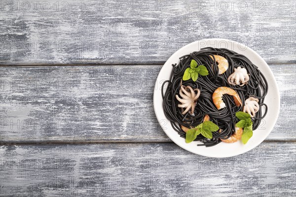 Black cuttlefish ink pasta with shrimps or prawns and small octopuses on gray wooden background. Top view, flat lay, copy space