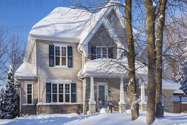 Country tan brick and vinyl cladded cottage style house facade with blue trim in winter, Quebec, Canada, North America