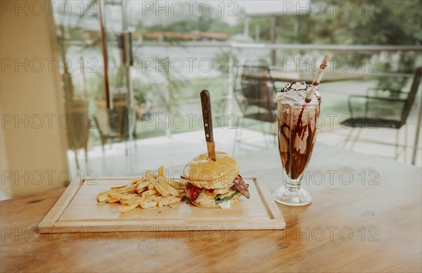 Classic burger with fries and milkshake on wooden board with copy space. Big hamburger with fries and milkshake on restaurant table