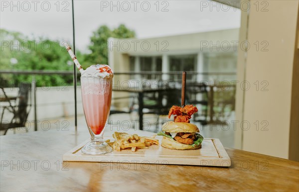 Traditional chicken burger with french fries and strawberry milkshake on restaurant table. Hamburger with french fries and strawberry milkshake on wooden table isolated