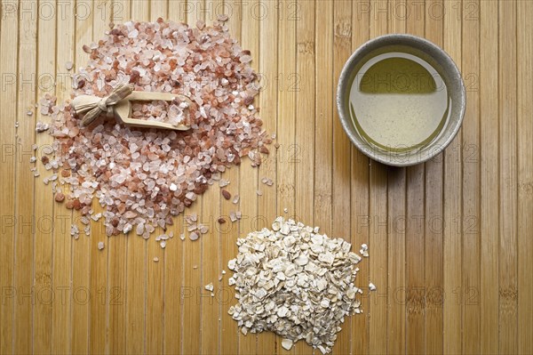 A flatlay studio photo of a pile of himalayan sea salt with a scoop, a pile of dried oatmeat, and a small bowl with olive oil