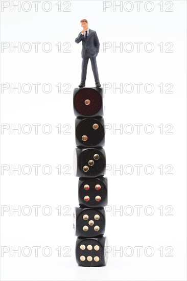 Symbol photo, man (figure) standing perplexed on a stack of dice showing the values 1 to 6 in ascending order