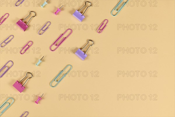 Stationery items like paper clips and drawing pins arranged on side of yellow background with empty copy space