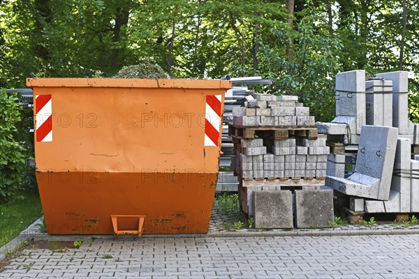 Orange industrial transportable dumpster container and cobble stones on palette at construction site