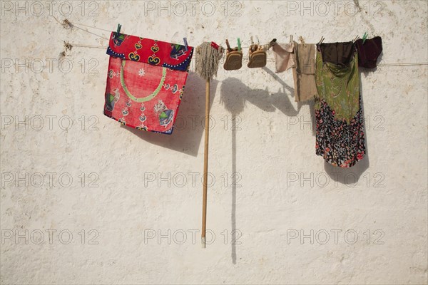 Clothes, shoes and a mop hanging to dry on a washing lineSilves, Algarve, Portugal, Washing line with colourful clothes and accessories in front of a white wall in the sunshine, Europe