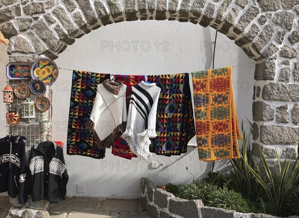 Souvenir sale in the spa town of Monchique, Algarve, Portugal, Traditional colourful textiles hang under a stone arch in the open air, accompanied by handicraft items, Europe