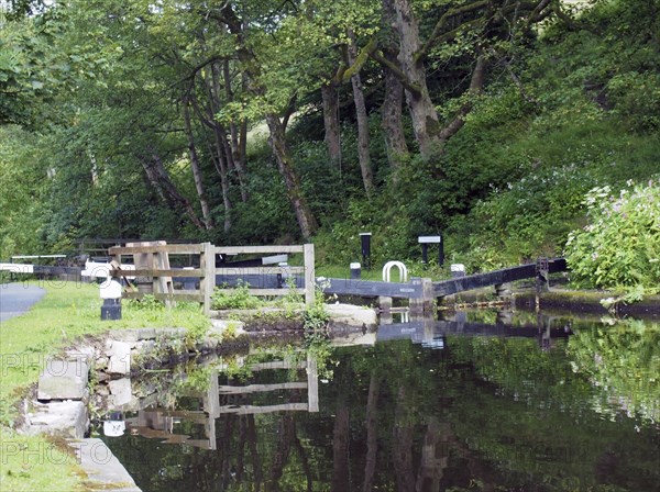 Old wooden lock gates with trees and flowers reflected in the water with mooring posts and fences on the rochdale canal at rawden mill near erringden near hebden bridge