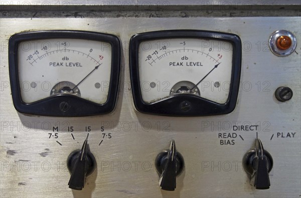 A close up of two old decibel meters on an old vintage reel to reel tape recorder with control knobs and switches