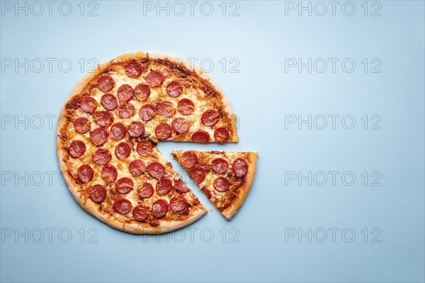 Pepperoni pizza on a blue background top view. Traditional italian food. Flatlay with a home-baked pizza with hot pepperoni and mozzarella