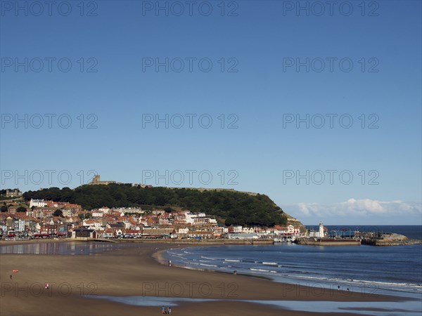 View of scarborough south bay with beach and town on a sunlit summer day with the harbour and castle in the distance