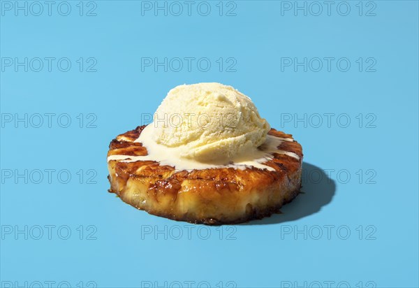 Summer dessert, roasted pineapple ring dipped in rum sauce, with a scoop of vanilla ice cream. Hawaiian dessert minimalist on a blue background