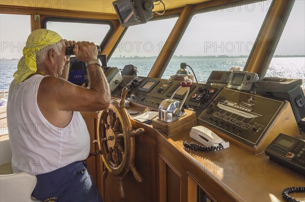 Captain in the post of a ship watching with binoculars on the Adriatic Sea along the town of Igea Marina near Rimini in Italy