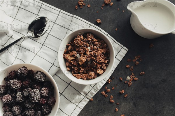 Frozen blackberries, granola, cream, towel on table. Blurred background.