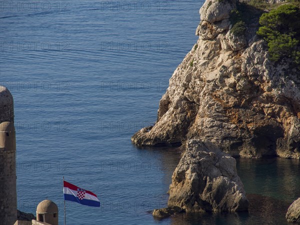 Rocks on the coast with a Croatian flag in the foreground and the sea in the background, Dubrovnik, Mediterranean Sea, Croatia, Europe