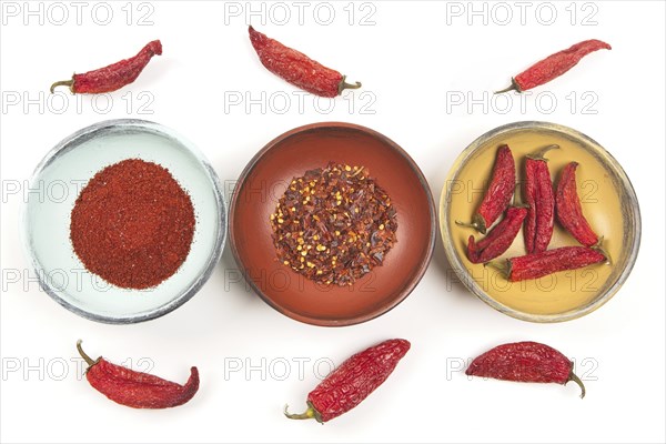 A flatlay photo of wooden bowls with whole peppers, red pepper powder, and red pepper flakes against a white background