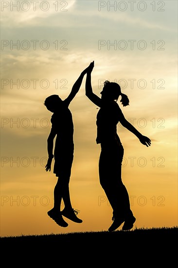 A boy and a teen girl jump up at sunset and give each other a high five