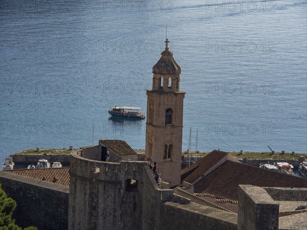 Narrow bell tower with a boat on the calm sea behind, dubrovnik, Mediterranean Sea, Croatia, Europe