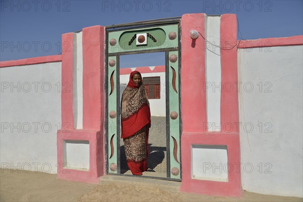 Nubian woman in typical bright dress, in front of her house, in the village of Umogaal in Dongola, Nile Valley, Nubia, Sudan, Africa