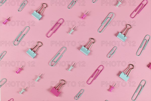 Stationery items like paper clips and drawing pins arranged on pink background