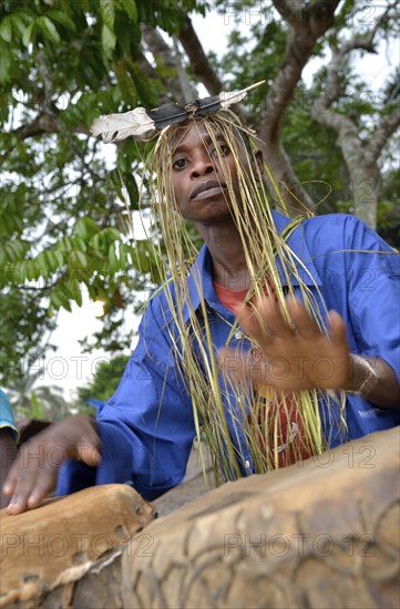 Musician with a headdress made of bast and a feather, playing drums, Nkala, Bandundu Province, Democratic Republic of the Congo