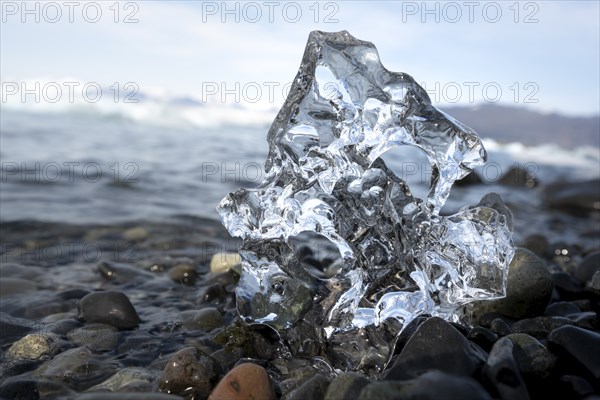 Ice, piece of ice with hole on black gravel beach, glacier lagoon Jökulsárlón, glacial lake, southern edge of Vatnajökull, southeast Iceland, Iceland, Europe