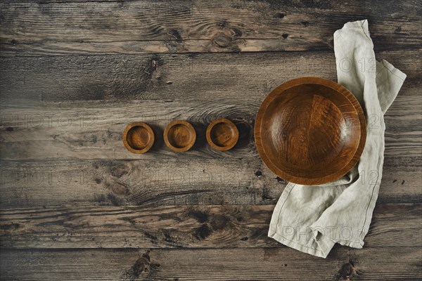 A large wooden bowl sits comfortably surrounded by three smaller bowls on a weathered wooden table. A soft, light linen cloth drapes beside them, creating a cozy, inviting atmosphere