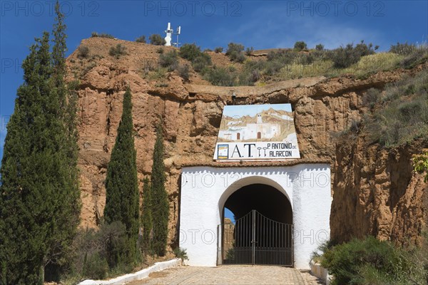 Entrance gate to a white building with a rock face and trees, surrounded by rustic charm on a sunny day, Pedro Antonio de Alarcon cave hotel, Guadix, Granada province, Andalusia, Spain, Europe