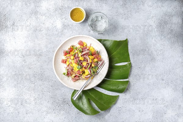 Tropical Hawaiian tahitian tuna mango salad on white plate on tropical monstera leafe