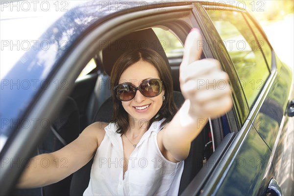 A smart looking middle-aged adult woman wearing sunglasses put her hand out the car window and raised her thumbs up